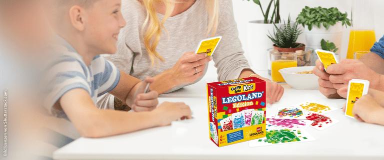 vierköpfige Familie spielt Karten, im Vordergrund Karten und Schachtel mit Legoland-Branding